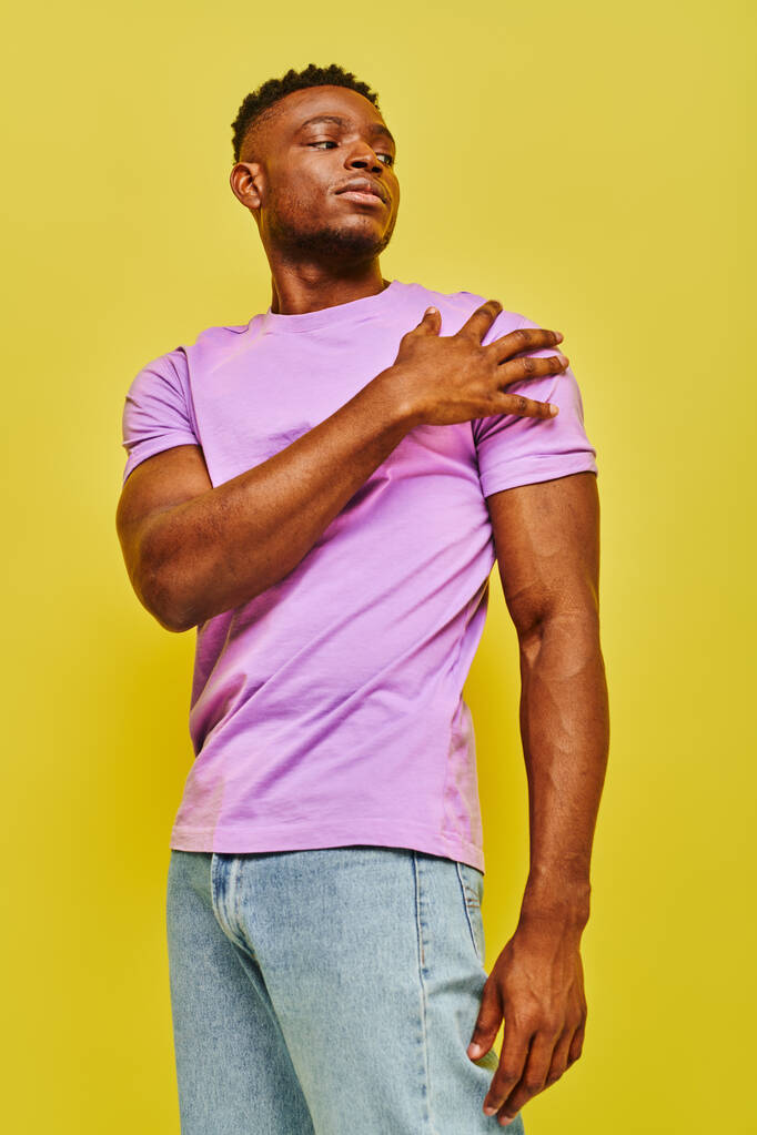 νεαρός αφρικανός με αυτοπεποίθηση, με έντονο μωβ μπλουζάκι που κοιτάζει αλλού στο κίτρινο φόντο. - Φωτογραφία, εικόνα