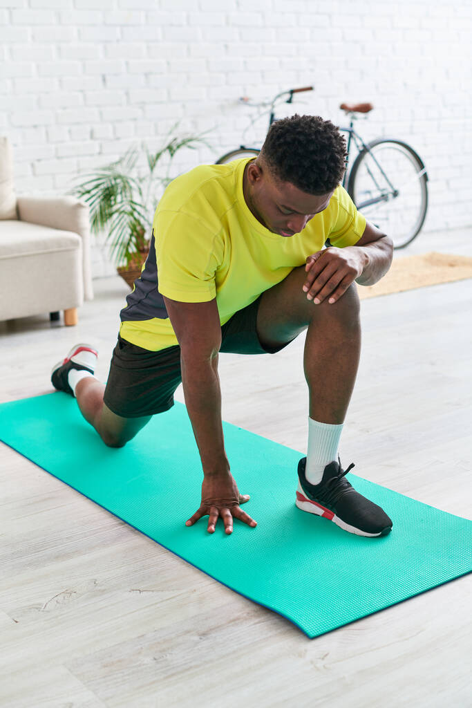 atletico uomo afroamericano in abbigliamento sportivo che si riscalda sul tappeto fitness in soggiorno a casa - Foto, immagini