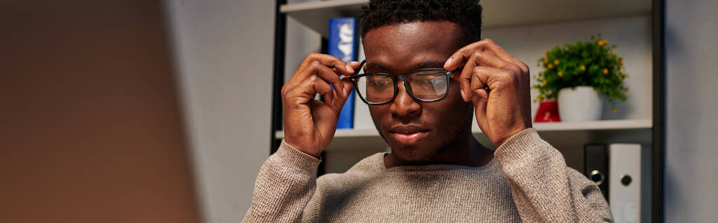 若いアフリカ系アメリカ人フリーランサーは,夜に自宅で働いている間に眼鏡を調整し,バナー - 写真・画像
