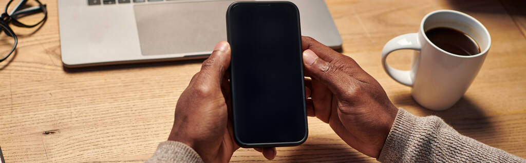 ラップトップ,バナーの近くに空白のスクリーンでスマートフォンを保持するアフリカ系アメリカ人の男性の見た目 - 写真・画像