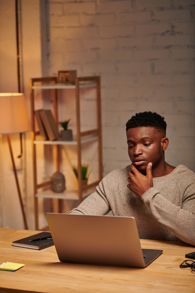 pensivo Africano americano freelancer olhando para laptop em casa escritório à noite, resolução de problemas - Foto, Imagem