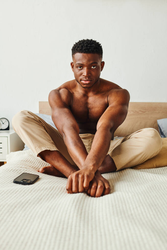 αυτοπεποίθηση και ισχυρή αφρικανική Αμερικανός άνθρωπος σε παντελόνι πιτζάμας κάθεται στο κρεβάτι και κοιτάζοντας την κάμερα - Φωτογραφία, εικόνα
