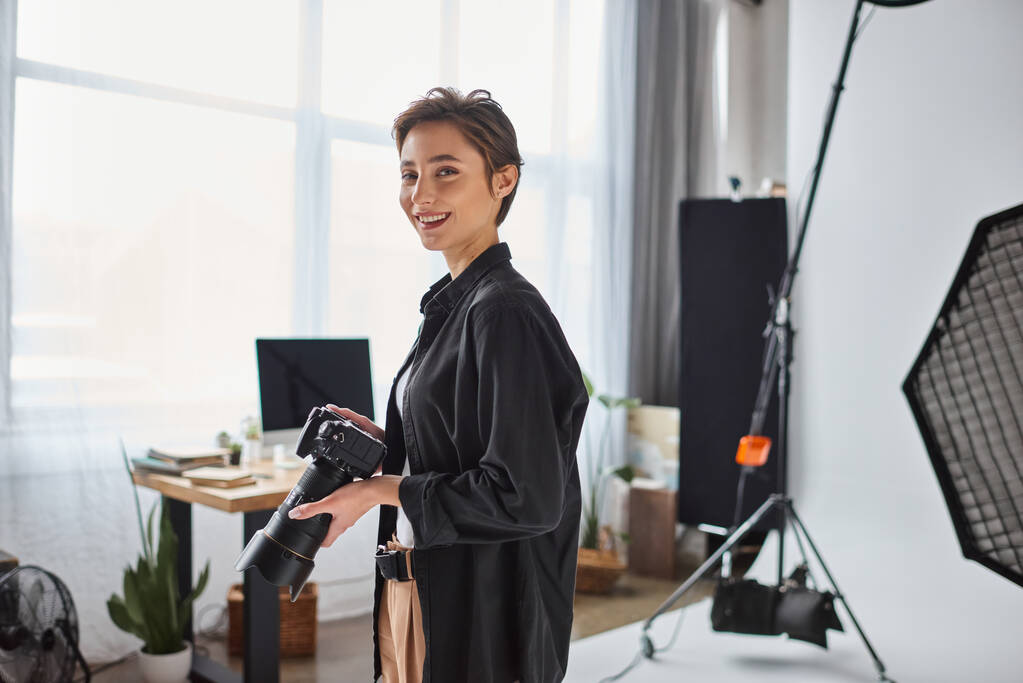 boldog fiatal női fotós rövid haj pózol vele kamera és mosolygós vidáman - Fotó, kép
