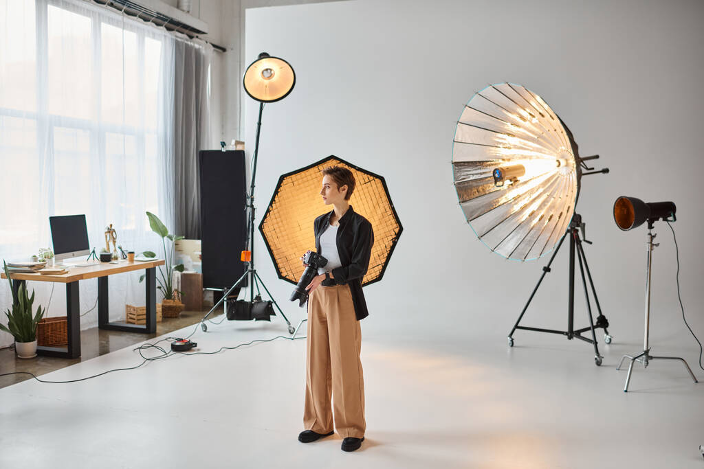 aantrekkelijke jonge vrouwelijke fotograaf in alledaagse outfit poseren in haar studio en wegkijken - Foto, afbeelding