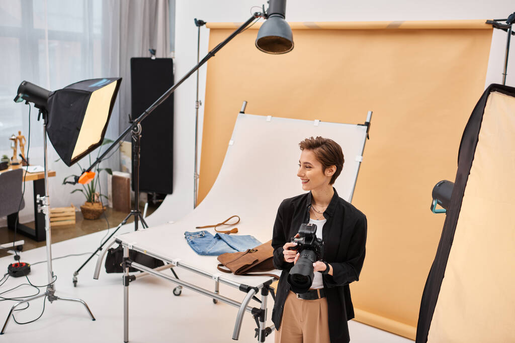 Günlük kıyafetleri içinde mutlu, çekici bir kadın fotoğrafçı stüdyosunda ekipmanlarıyla çalışıyor. - Fotoğraf, Görsel