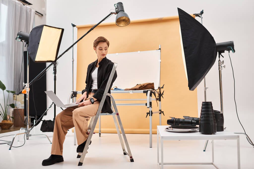 очаровательный коротковолосый фотограф сидит и ретуширует фотографии в своей студии с помощью ноутбука - Фото, изображение