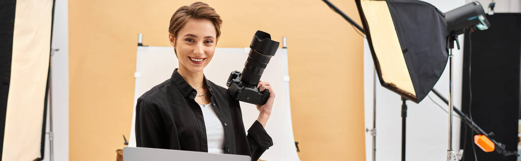 fröhliche hübsche Frau, die glücklich lächelt, während sie Fotos retuschiert und ihre Kamera im Studio hält, Banner - Foto, Bild