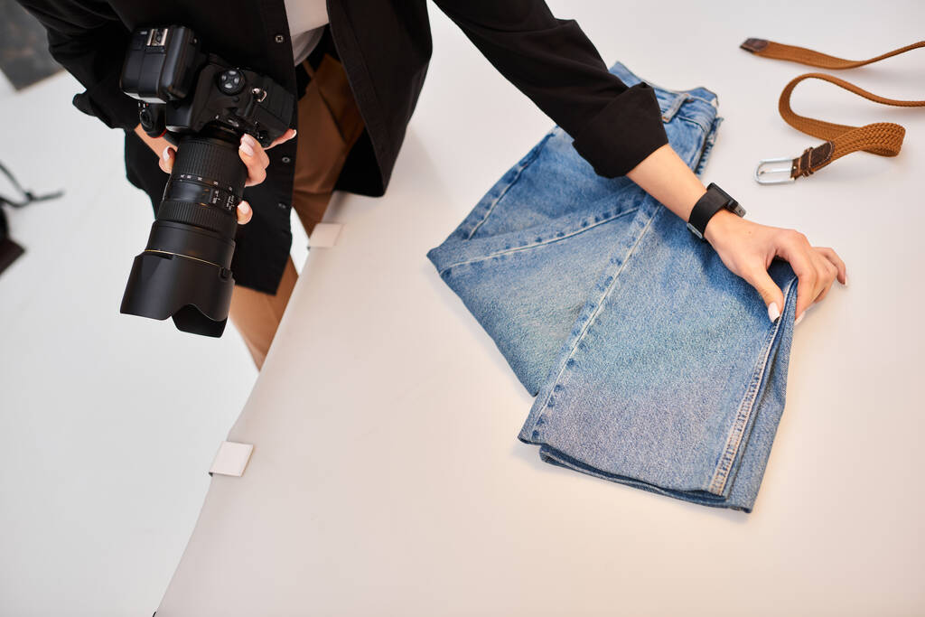 przycięty widok młodej fotografki przygotowującej się do zrobienia zdjęć obiektów z jeansów i brązowego pasa - Zdjęcie, obraz
