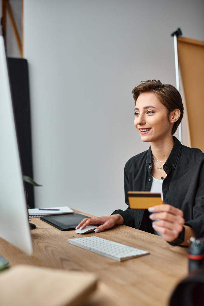 heureux attrayant photographe femme payant en ligne en utilisant sa carte de crédit et souriant joyeusement - Photo, image
