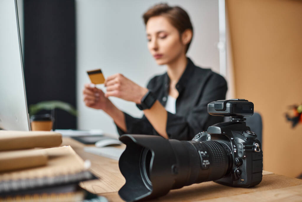 enfoque en la cámara en la mesa junto a la joven fotógrafa borrosa que paga en línea con tarjeta de crédito - Foto, Imagen