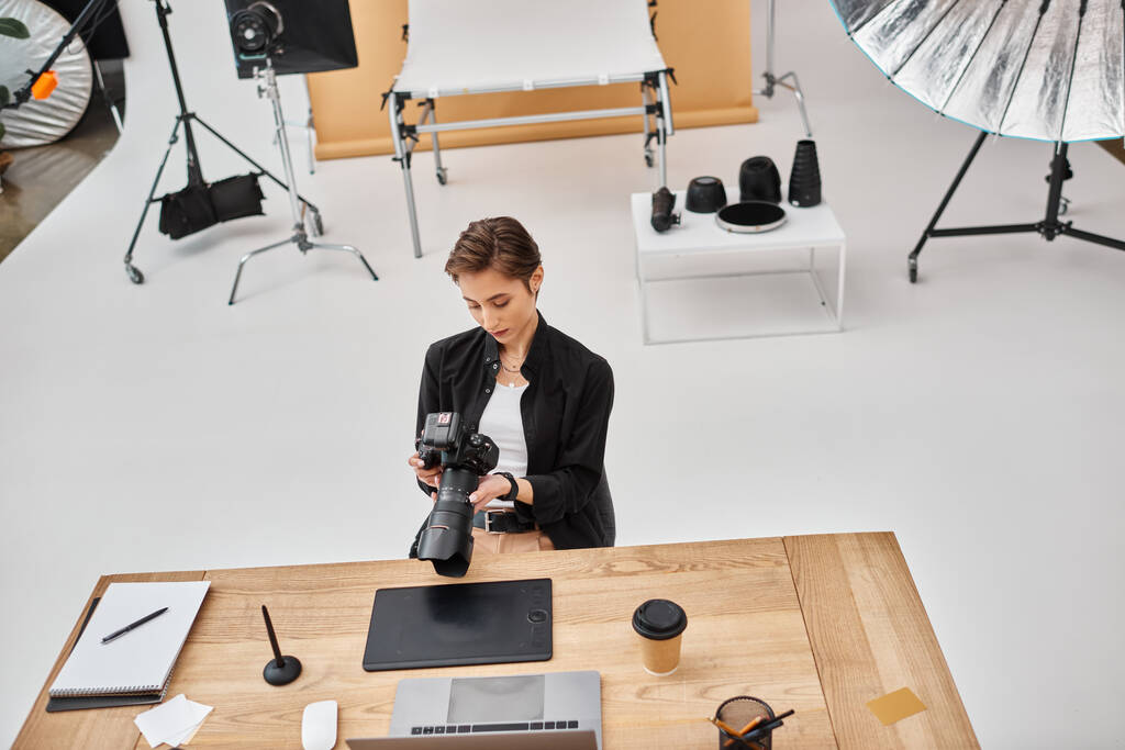 aantrekkelijke professionele vrouwelijke fotograaf in casual kleding werken met haar camera in studio - Foto, afbeelding