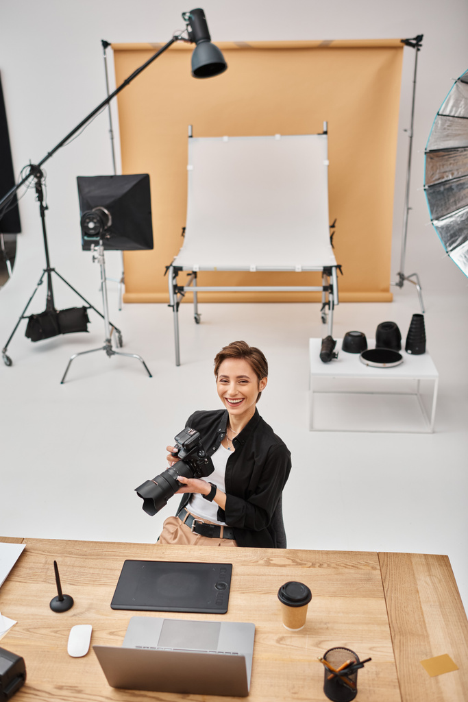 cheerful professional woman in casual attire smiling at camera working at her workplace in studio - Photo, Image