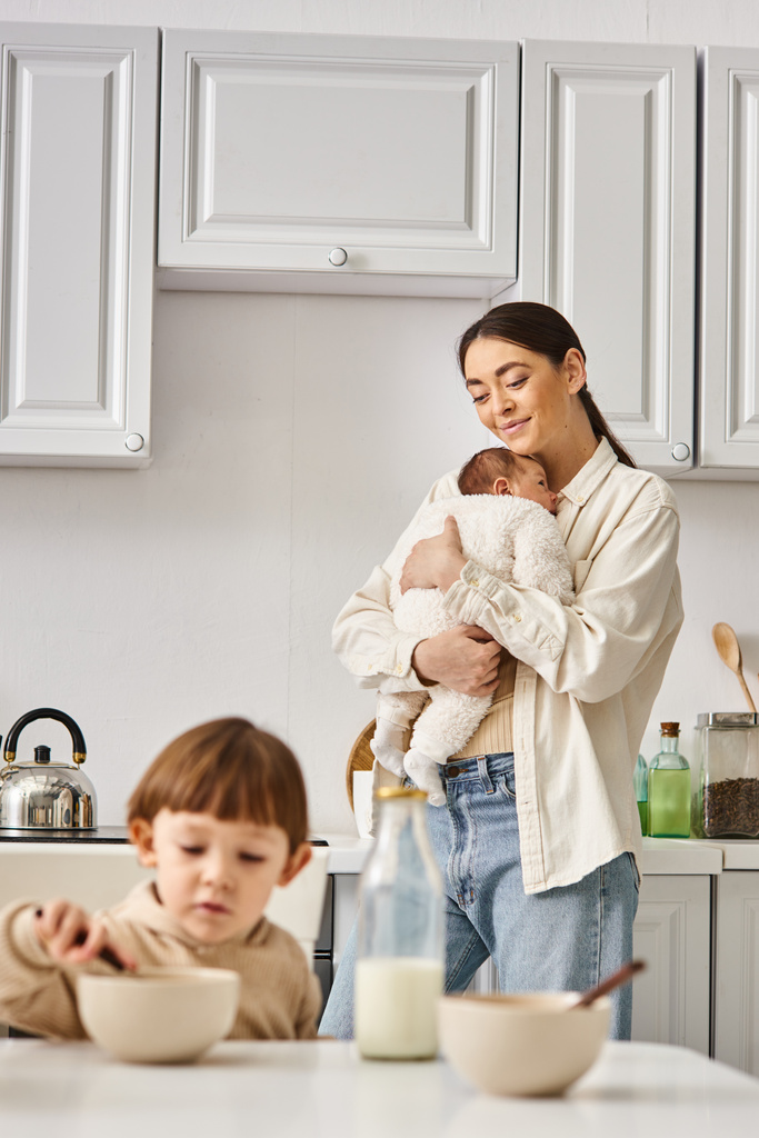 allegra madre amorevole posa accanto al suo bambino figlio con neonato in mano durante la colazione - Foto, immagini