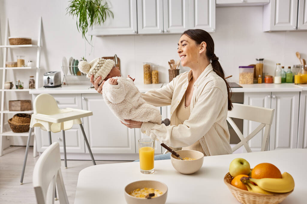 veselá atraktivní žena v domácím oblečení drží její roztomilé dítě chlapce při snídani, moderní rodičovství - Fotografie, Obrázek