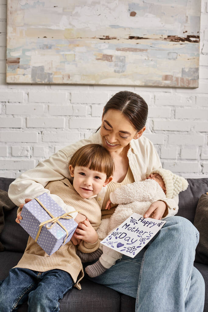 mulher bonita sentada no sofá com seus filhos com presente e cartão de saudação no dia das mães - Foto, Imagem