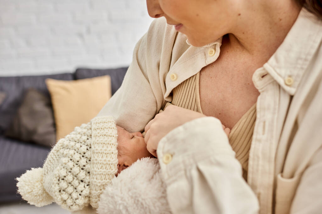привлекательная заботливая радостная мать в уютной домашней одежде кормящая грудью своего новорожденного ребенка, современное воспитание - Фото, изображение