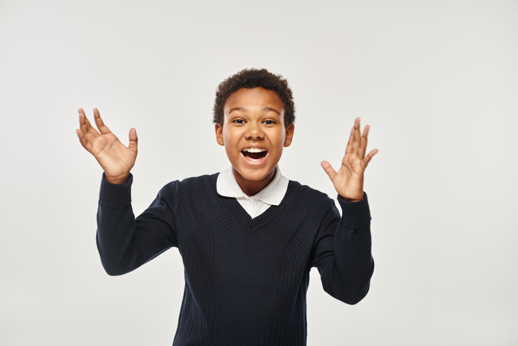 excited african american boy in school uniform rejoicing while looking at camera on grey backdrop - Photo, Image