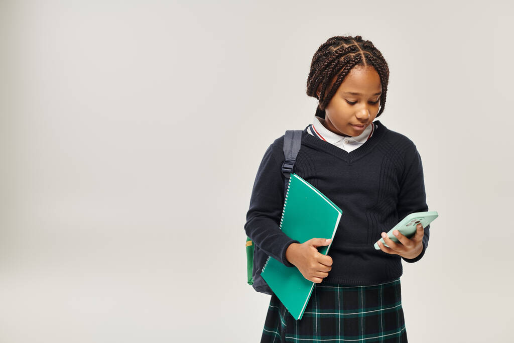 американская школьница в форме с помощью смартфона и с ноутбуком на сером - Фото, изображение