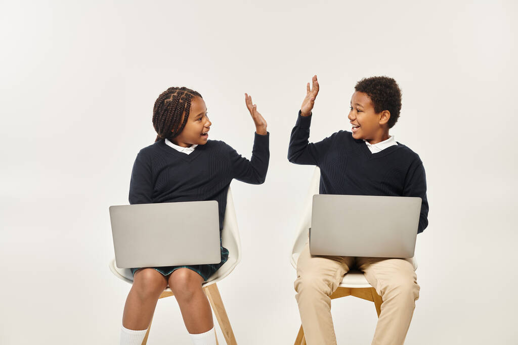 boldog afro-amerikai iskolások egyenruhás laptopok és így pacsi szürke háttér - Fotó, kép