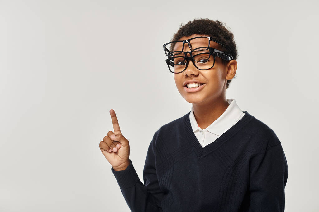 ottimistico scolaro afroamericano in occhiali che tiene gli occhiali e guarda la fotocamera sul grigio - Foto, immagini