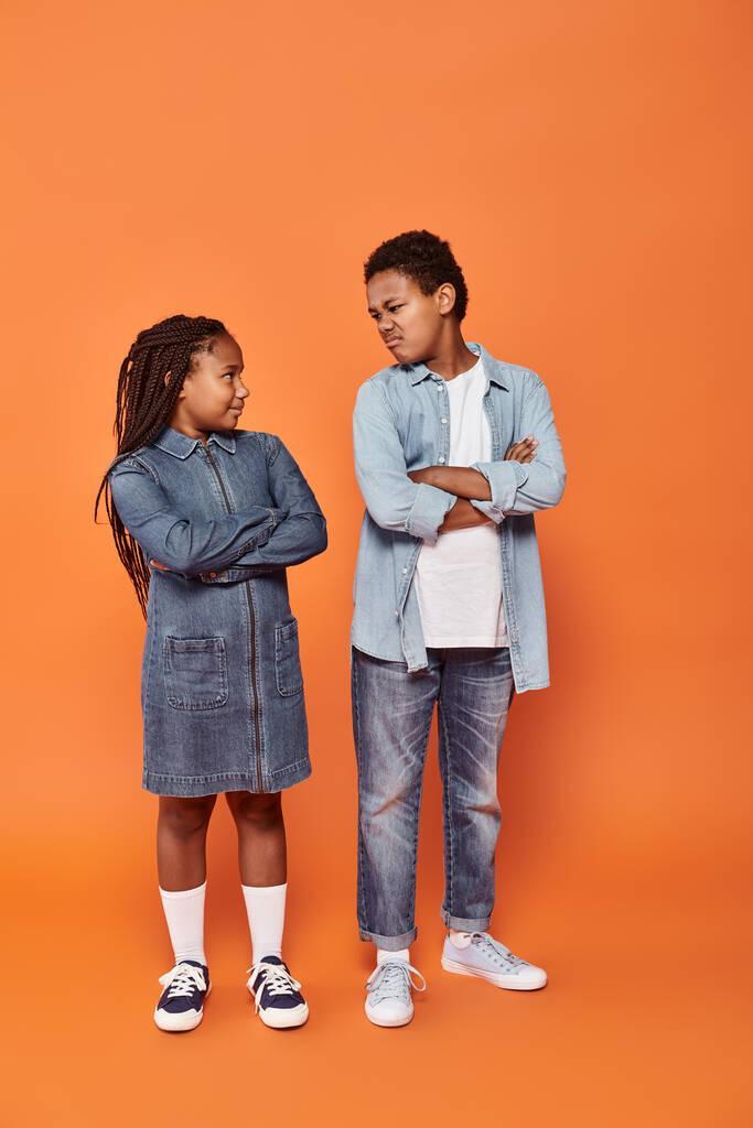 Afrikanisch-amerikanische Kinder in lässiger Jeans-Kleidung posieren mit verschränkten Armen auf orangefarbenem Hintergrund - Foto, Bild