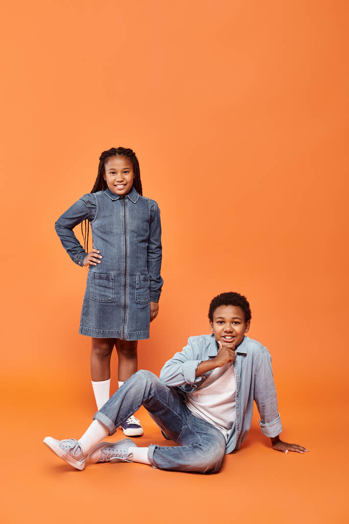 веселый африканский американец и девушка позируют вместе на оранжевом фоне и улыбаются камеру - Фото, изображение