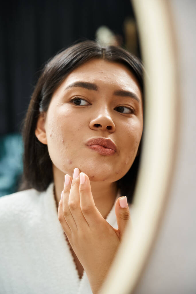 jeune fille asiatique avec des cheveux bruns examiner son visage avec de l'acné dans le miroir de salle de bains, problème de peau - Photo, image