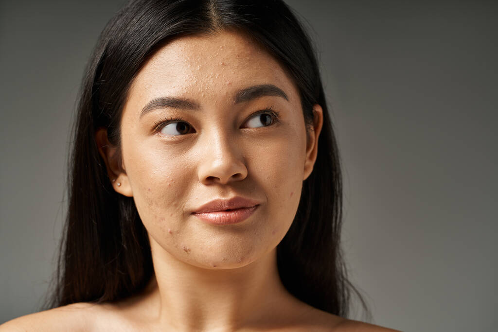 Esmer saçlı, sivilceli genç Asyalı kadın banyodaki aynaya bakıyor. - Fotoğraf, Görsel