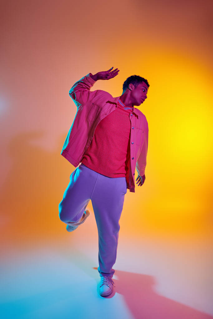 Stijlvolle Afrikaanse Amerikaanse man in trendy kleding met levendige gradiënt achtergrond, dynamische pose - Foto, afbeelding