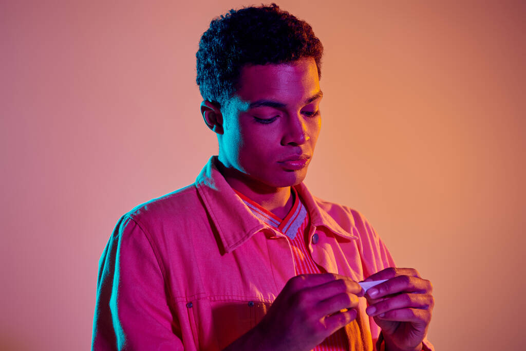 african american man preparing cigarette for smoking on vibrant background with blue lighting - Photo, Image