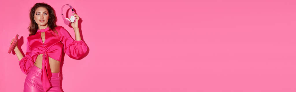 hermosa muñeca como mujer en top de la cosecha y pantalones de color rosa de pie con auriculares y bolso brillante, bandera - Foto, imagen