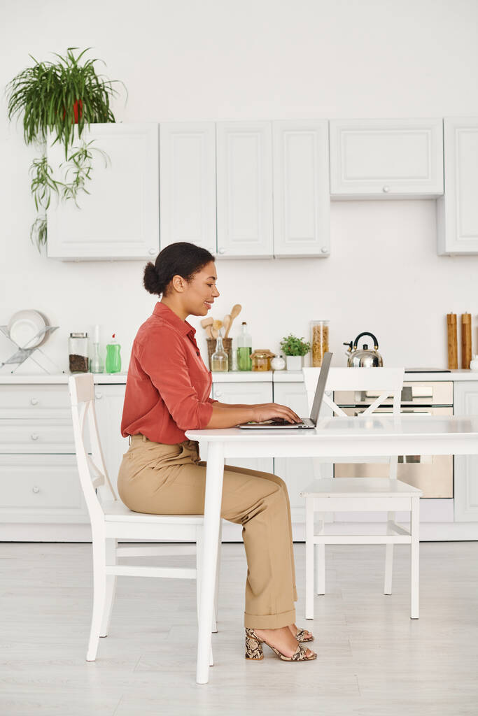 задоволений афроамериканський дієтолог, використовуючи ноутбук, працюючи дистанційно з її сучасної кухні - Фото, зображення