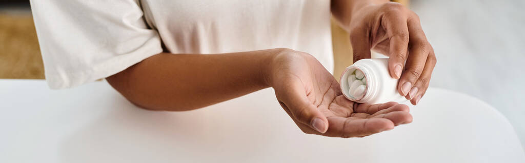 dietista afroamericano recortado verter píldoras en la palma de la mano de la botella de medicamentos, pancarta - Foto, imagen