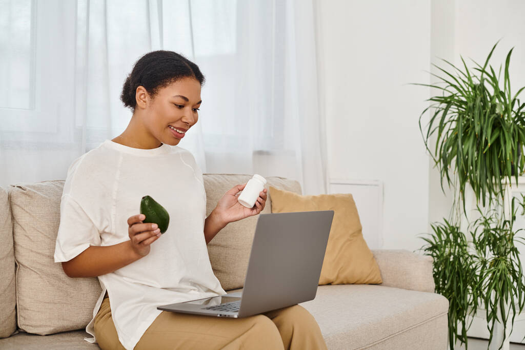 felice nutrizionista afroamericano con integratori e avocado dando consigli dietetici tramite laptop - Foto, immagini