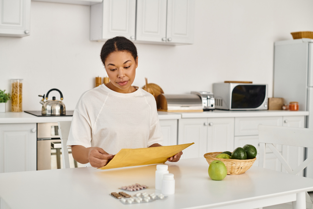 брюнетка африканская американка открывает конверт с диетическим планом рядом с добавками и фруктами - Фото, изображение