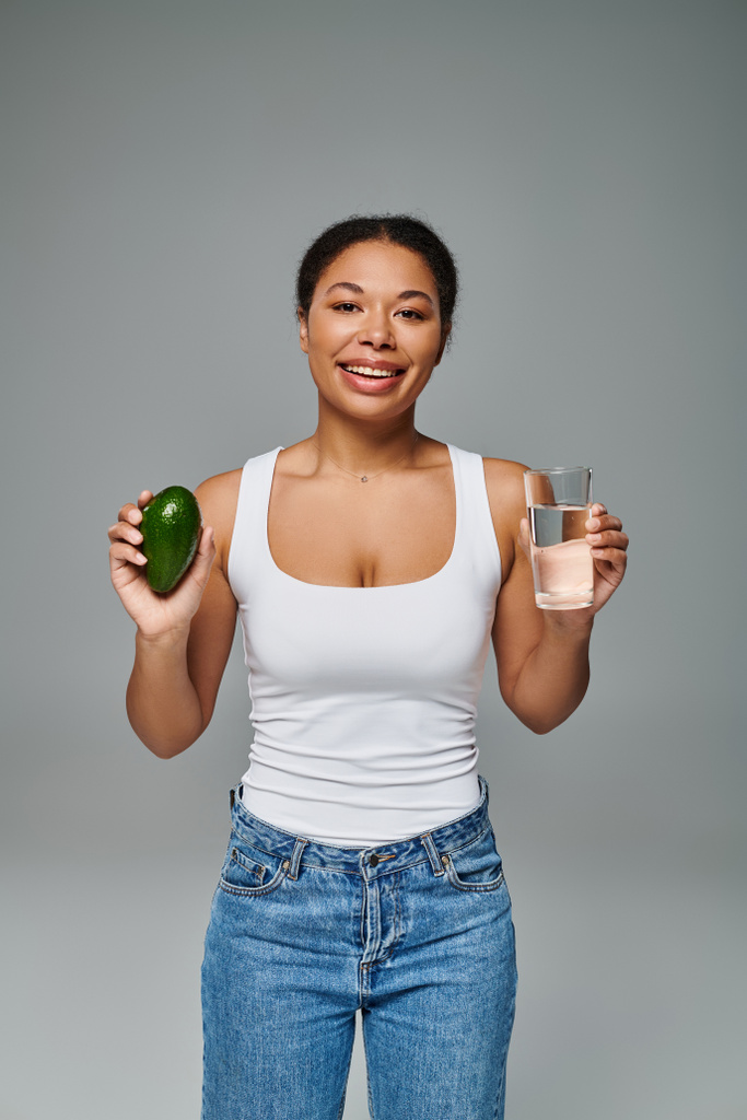 feliz nutricionista afro-americano promovendo hidratação e alimentação saudável com abacate e água - Foto, Imagem