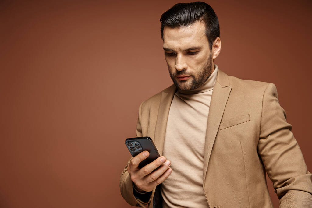 knappe zakenman in elegante kleding controleren van zijn smartphone op beige achtergrond, aangesloten - Foto, afbeelding