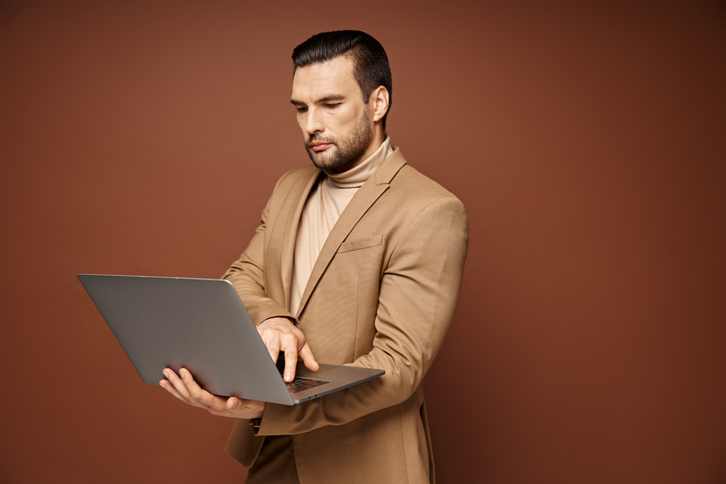 määrätietoinen ja komea ammattilainen käyttää hänen laptop työskennellessään etänä beige tausta - Valokuva, kuva
