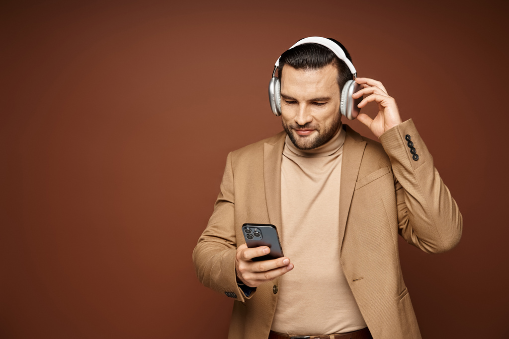 χαμογελαστός όμορφος άντρας με ασύρματα ακουστικά χρησιμοποιώντας το smartphone του σε μπεζ φόντο, ψηφιακή εποχή - Φωτογραφία, εικόνα