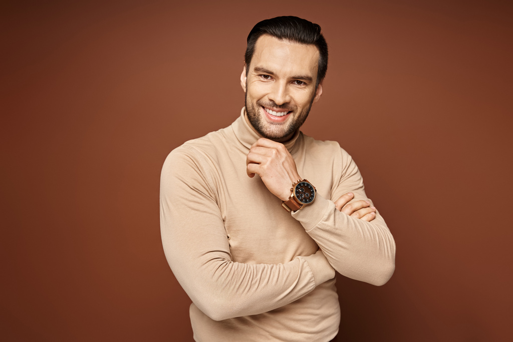 happy man with bristle posing in turtleneck and touching his chin on beige background, male model - Photo, Image