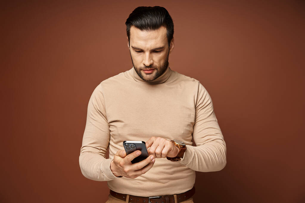 Boğazlı kazaklı yakışıklı adam bej arka planda akıllı telefonunu kullanıyor, sosyal medya... - Fotoğraf, Görsel