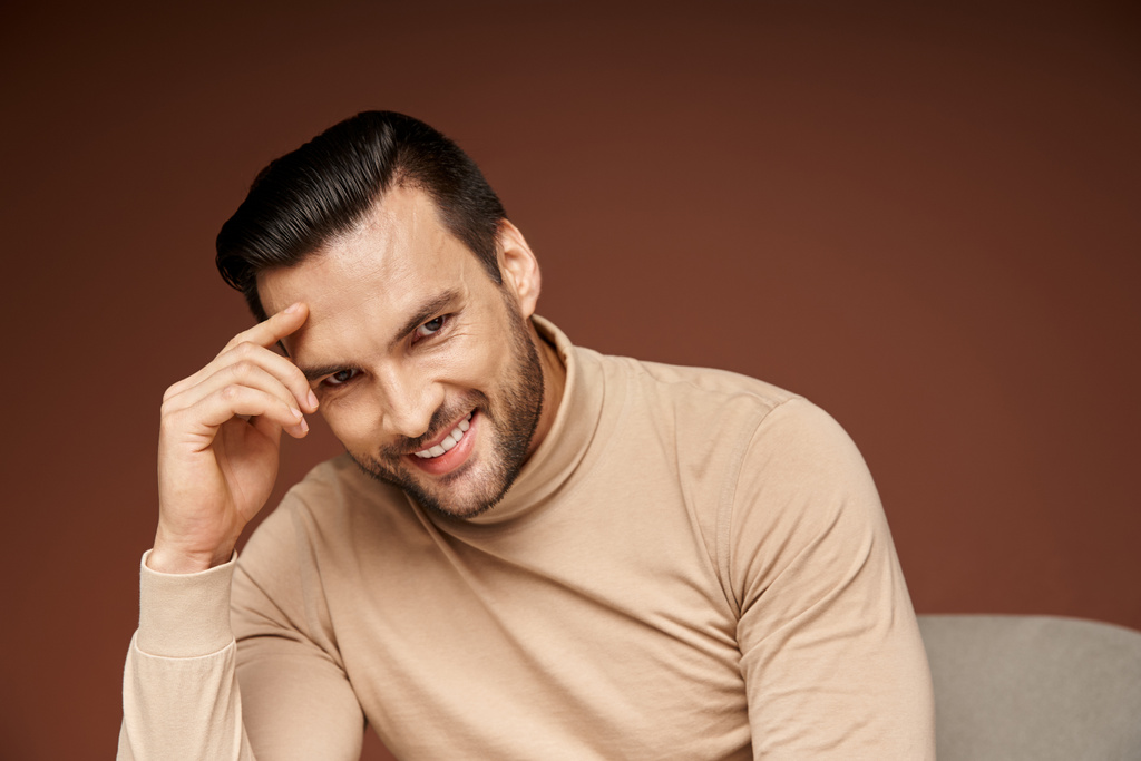 portrait of handsome man in turtleneck looking at camera and smiling on beige background - Photo, Image