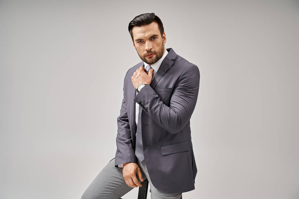 bell'uomo d'affari in elegante abbigliamento formale appoggiato sullo sgabello alto su sfondo grigio, business - Foto, immagini