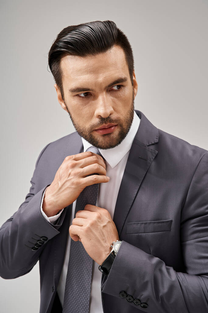 гарний чоловік у формальному одязі, що регулює краватку на сірому фоні, корпоративна мода - Фото, зображення