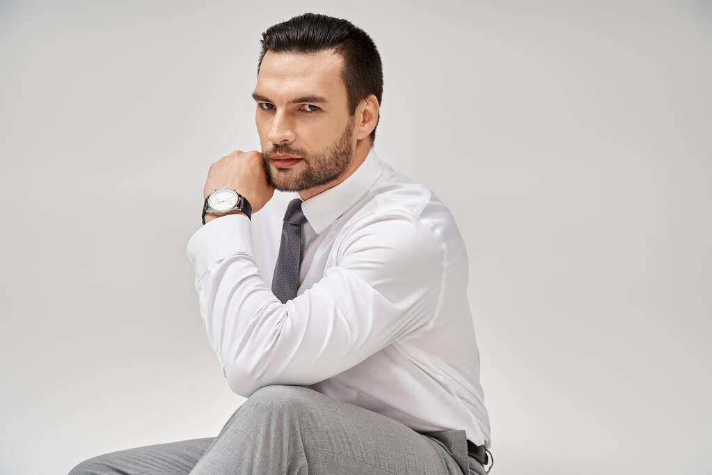good looking businessman in elegant formal wear sitting on floor in studio with grey background - Photo, Image