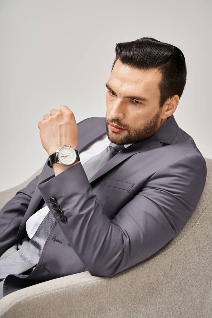retrato de empresario pensativo en traje elegante sentado en sillón cómodo sobre fondo gris, 30s - Foto, Imagen