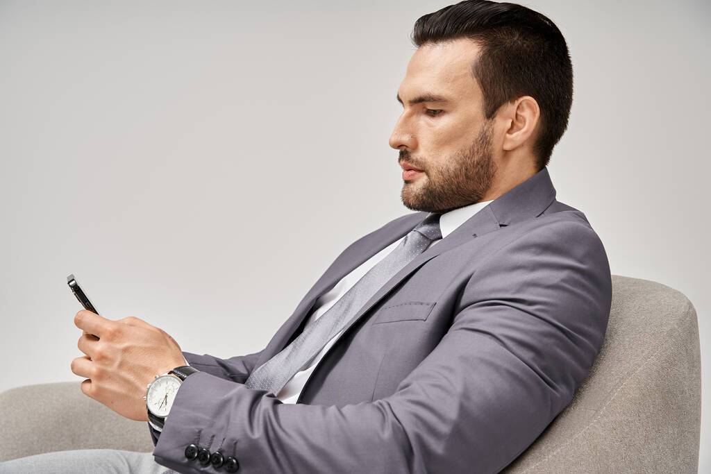 uomo d'affari con setole seduto sulla poltrona e utilizzando smartphone su sfondo grigio, social media - Foto, immagini