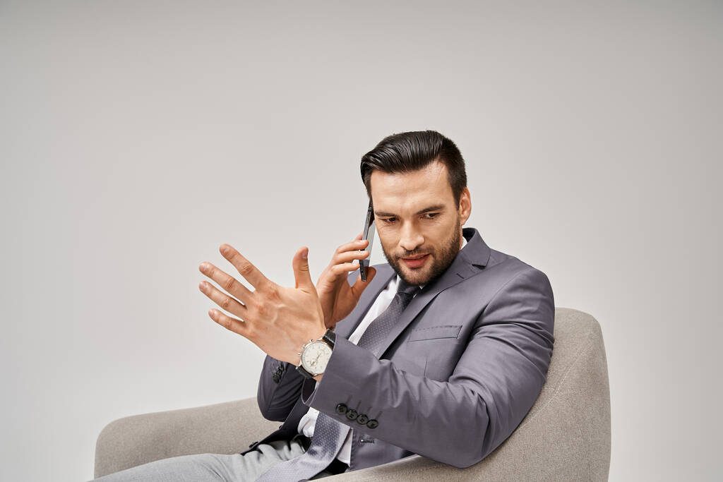 Geschäftsmann mit Borsten auf Sessel sitzend und Smartphone auf grauem Hintergrund - Foto, Bild