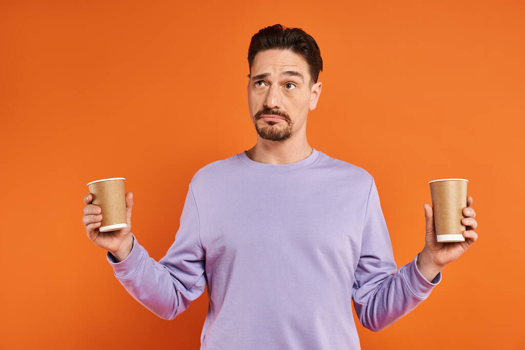 бородатий чоловік у фіолетовому светрі тримає паперові стаканчики з кавою, щоб піти на помаранчевий фон, вибір - Фото, зображення