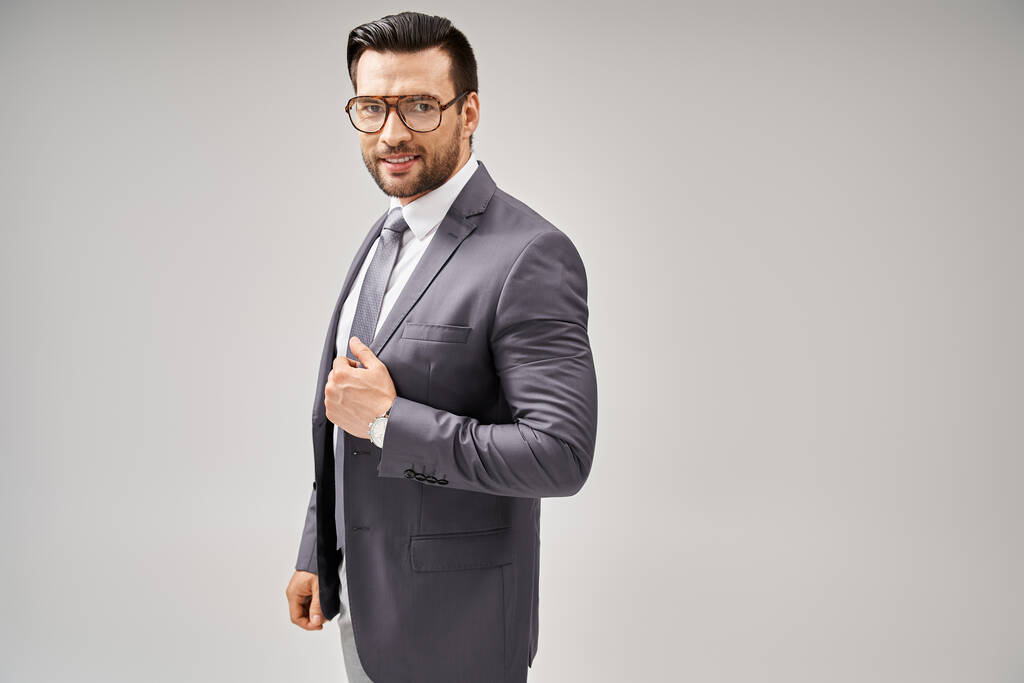 hombre de negocios alegre en ropa formal y gafas de pie sobre fondo gris, elegancia y estilo - Foto, Imagen